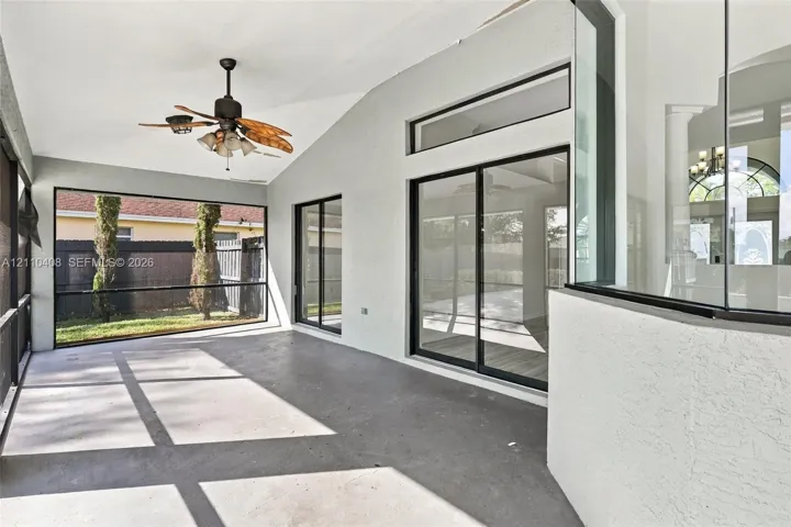 Screened-in patio featuring concrete flooring, a vaulted ceiling, a ceiling fan with integrated lighting, and multiple sliding glass door access points