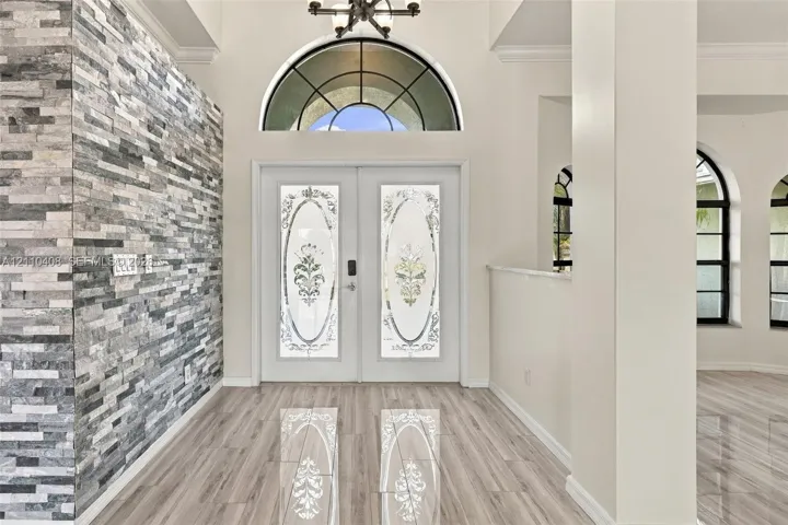 Entryway featuring a stacked stone accent wall, double doors with decorative glass inserts, a semicircular transom window, and wood-finish flooring