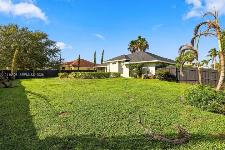 Expansive backyard featuring a sprawling grass lawn, mature palm trees, professional landscaping, and perimeter wood fencing