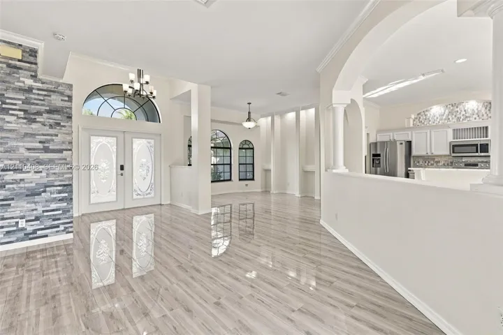 Polished tile flooring, stacked stone feature wall, arched windows, grand double-door entrance with decorative glass, and architectural columns