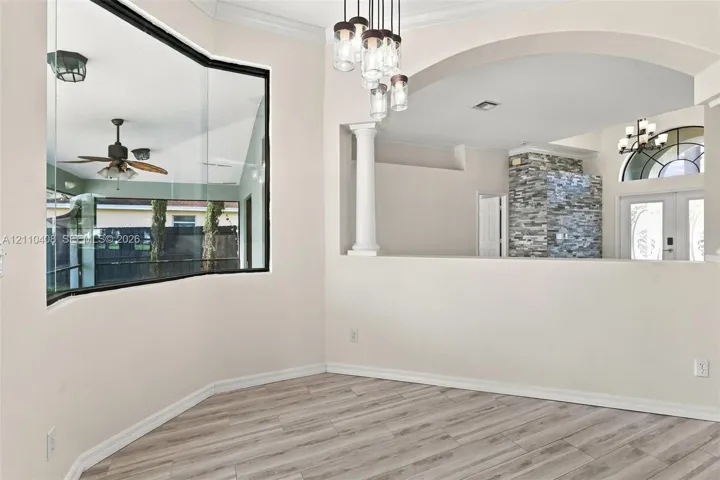Bay window featuring floor-to-ceiling glass, wood-finish flooring, architectural column, arched wall opening, and multi-light pendant fixture