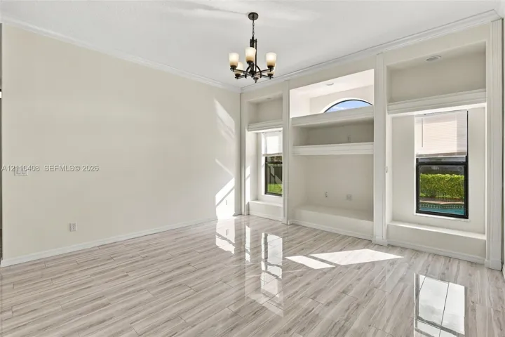 Room featuring wood-finish tile flooring, custom built-in cabinetry, crown molding, and a central multi-light chandelier
