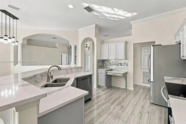 Kitchen featuring quartz countertops, wood-finish flooring, stainless steel appliances, decorative tile backsplash, and arched architectural detailing