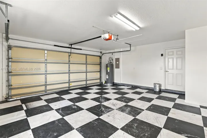 Garage featuring a black and white checkered floor, automatic garage door opener, overhead fluorescent lighting, and an internal water heater