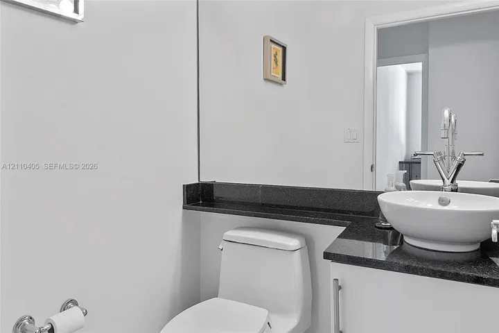 Vanity with a white vessel sink, dark stone countertop, white cabinetry, chrome faucet, and wall-to-wall mirror