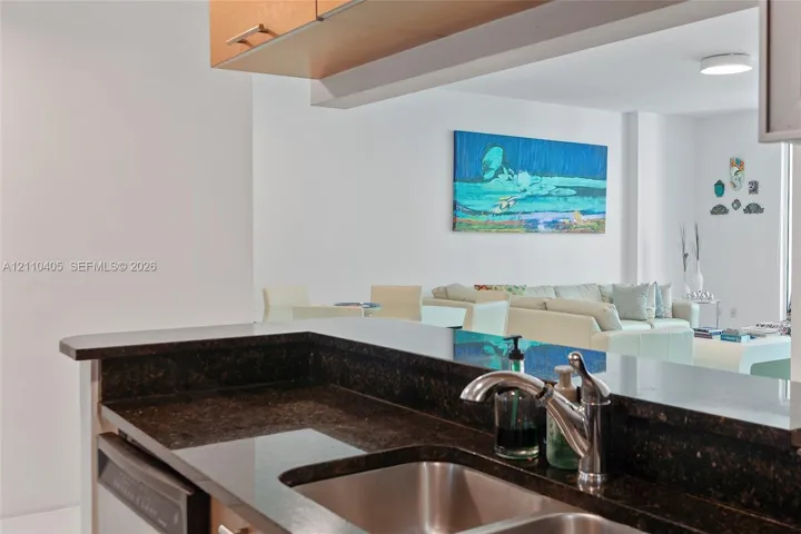 Kitchen featuring dark stone countertops, undermount stainless steel sink, polished chrome gooseneck faucet, and natural wood-tone cabinetry