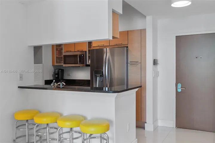 Kitchen featuring a pass-through breakfast bar with stone surfacing, stainless steel appliances, and wood-finish cabinetry