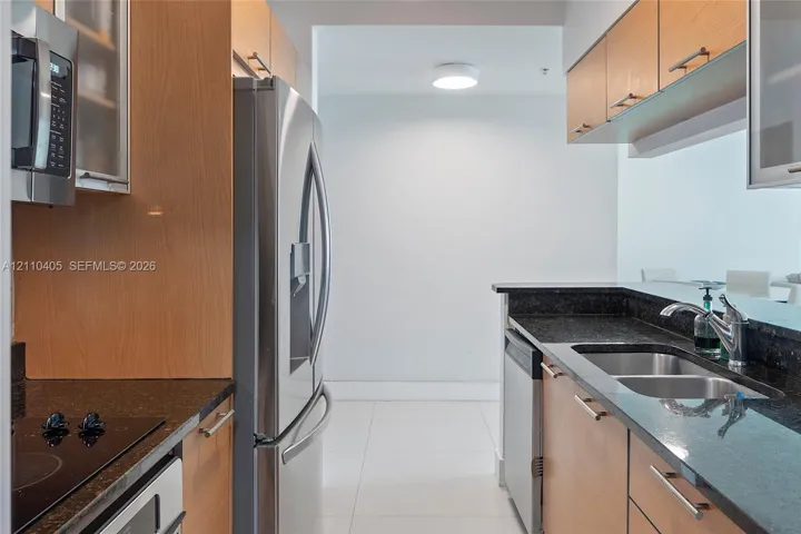 Kitchen featuring wood-veneer cabinetry, stone countertops, stainless steel appliances, and a dual-basin undermount sink