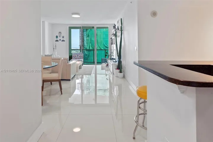 Open-concept interior featuring large-format polished tile flooring, a kitchen breakfast bar with a dark stone countertop, and floor-to-ceiling glass sliding doors