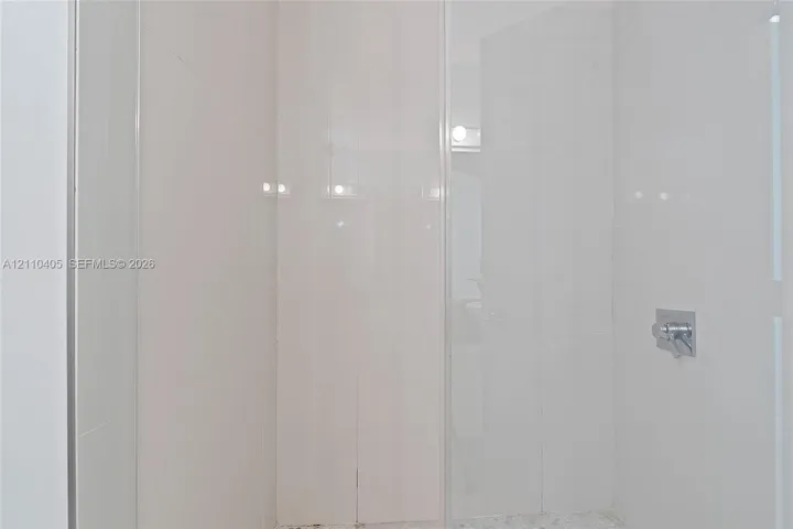 Walk-in shower enclosure with full-height white tile wall surround, glass door, and polished chrome fixtures