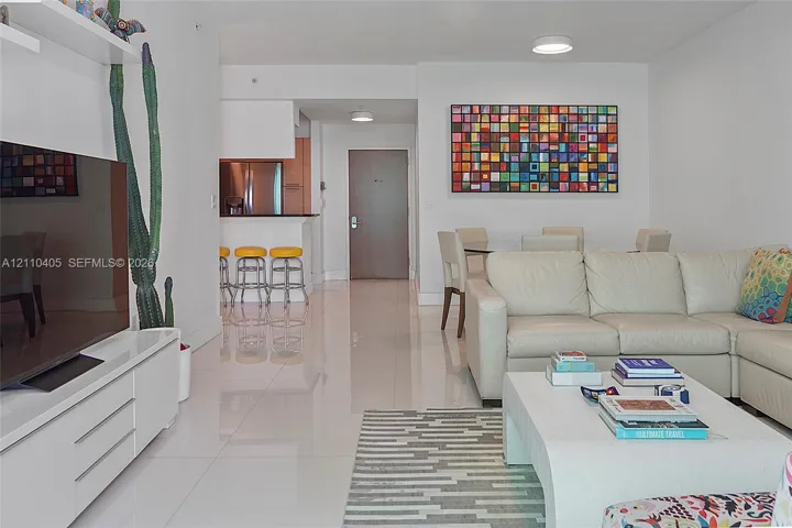 Glossy tile flooring, built-in wall-mounted media console, and kitchen breakfast bar with overhead recessed lighting