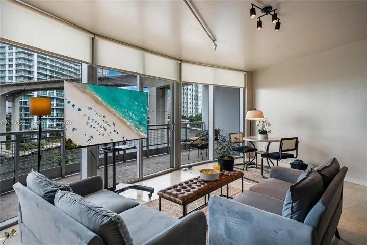 Floor-to-ceiling windows with retractable shades, polished tile flooring, industrial-style track lighting, and a private balcony with metal railings