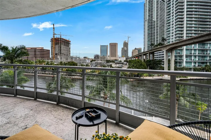 Covered balcony featuring stone flooring and metal railings with wire mesh inserts, overlooking the waterfront and surrounding cityscape