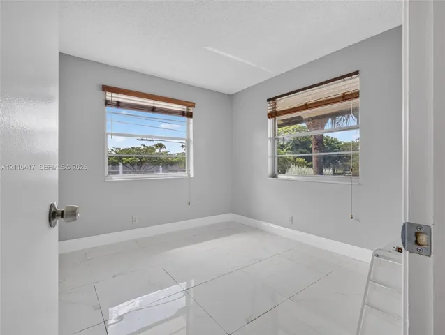Neutral-toned interior featuring large-format tile flooring, textured ceilings, and dual windows with built-in horizontal blinds