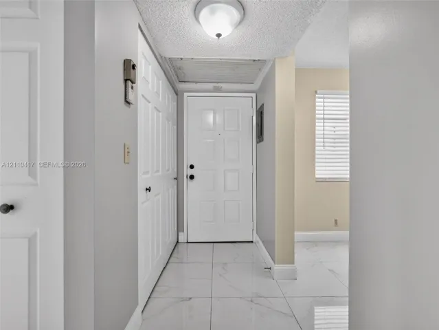 Entryway featuring large-format white tile flooring, paneled white interior doors, a flush-mount ceiling fixture, and a white paneled exterior door