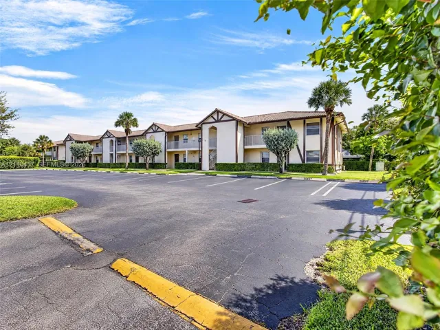 Two-story building featuring a neutral stucco exterior, brown trim, multi-gabled roofline, private balconies, and dedicated asphalt parking