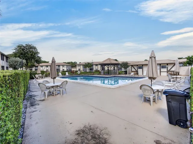 In-ground swimming pool featuring a concrete deck, built-in gazebo, and manicured hedge perimeter