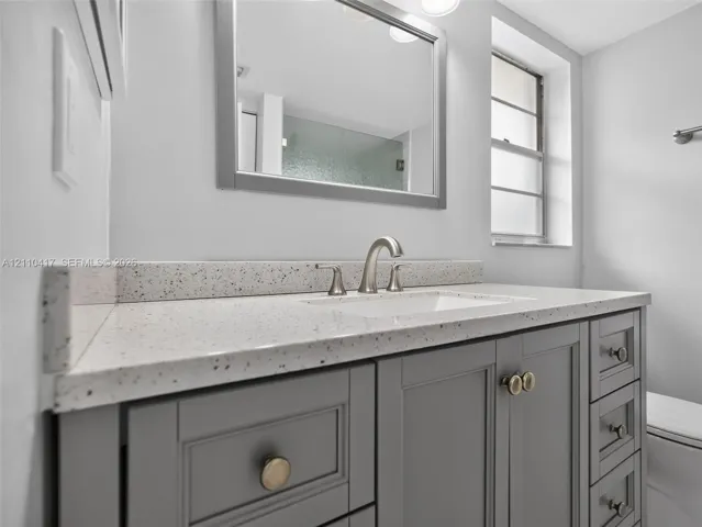 Grey shaker-style vanity featuring a light-toned speckled countertop, undermount sink, brushed nickel faucet, and integrated mirror