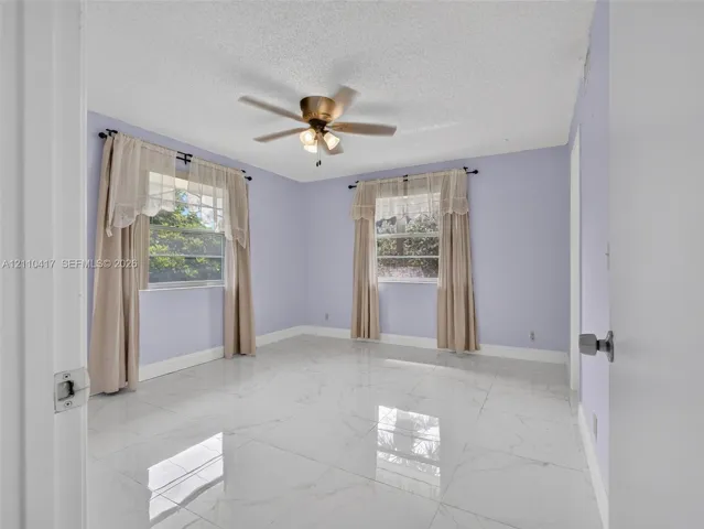 Large-format polished tile flooring, ceiling fan with integrated lighting, and multiple windows providing natural light