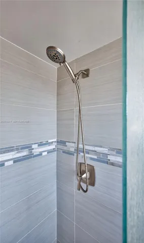 Shower enclosure featuring brushed nickel handheld showerhead, single-handle pressure balance valve, horizontal neutral-toned wall tile, and decorative glass mosaic accent border