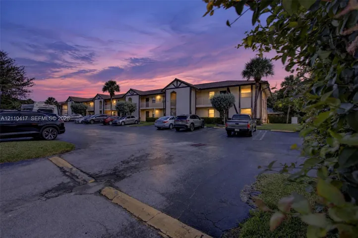 Multi-level building exterior featuring a stucco facade with dark trim accents, a tile roof, covered entryways, and designated asphalt parking