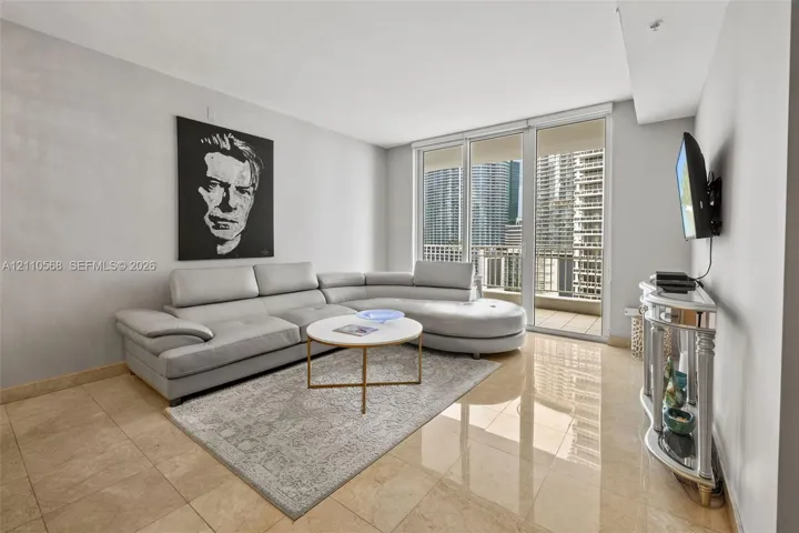 Living area featuring neutral-toned tile flooring, floor-to-ceiling glass panel doors, and an attached balcony
