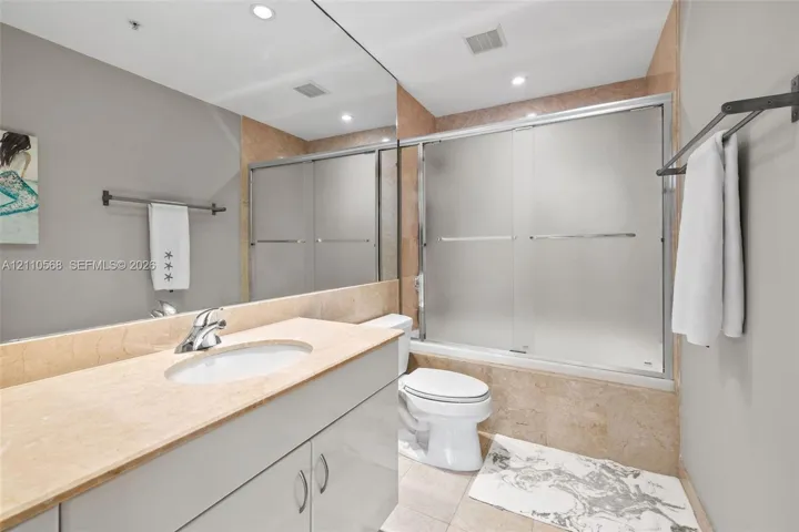 Bathroom featuring a vanity with a stone countertop, an integrated sink, full-width wall mirror, and a tub-shower combination with sliding frosted-glass doors