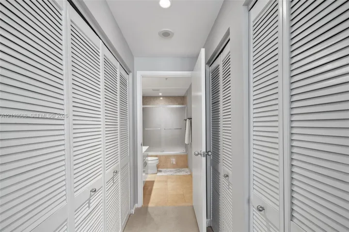Hallway featuring white louvered-style closet doors, recessed ceiling lighting, and tile flooring