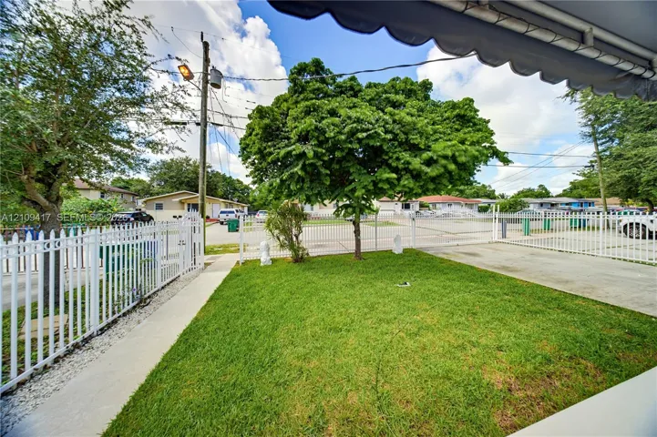 Enclosed outdoor area featuring a manicured lawn, white metal perimeter fencing, concrete hardscaping, and mature landscaping