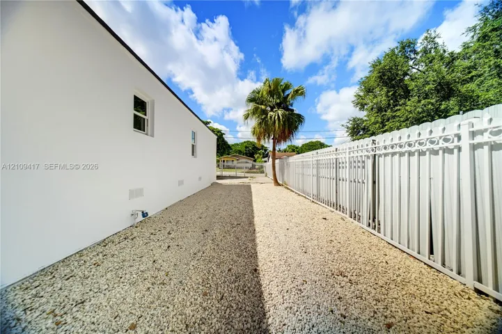 Side yard with white exterior wall, gravel ground cover, and full-height white vinyl privacy fencing