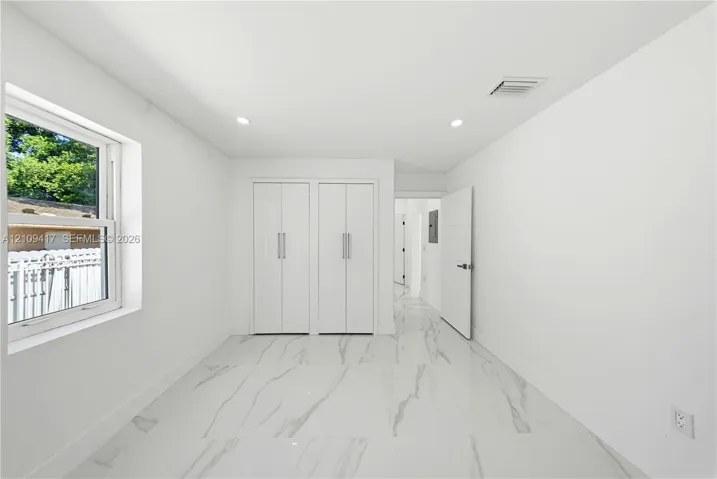Interior room featuring large-format stone-finish tile flooring, dual built-in floor-to-ceiling closets with minimalist hardware, recessed lighting, and a single-hung window
