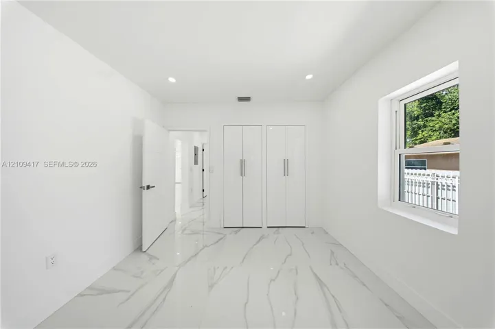 Interior space featuring large-format veined porcelain tile flooring, dual glossy white closet doors with vertical bar pulls, recessed lighting, and a dual-pane window