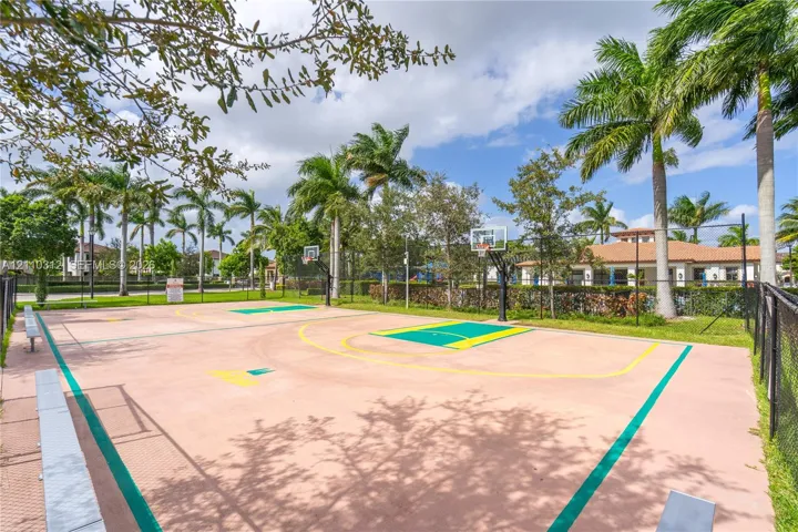 Outdoor basketball court featuring paved surfacing, dual goals, and perimeter fencing, accented by palm trees and manicured landscaping