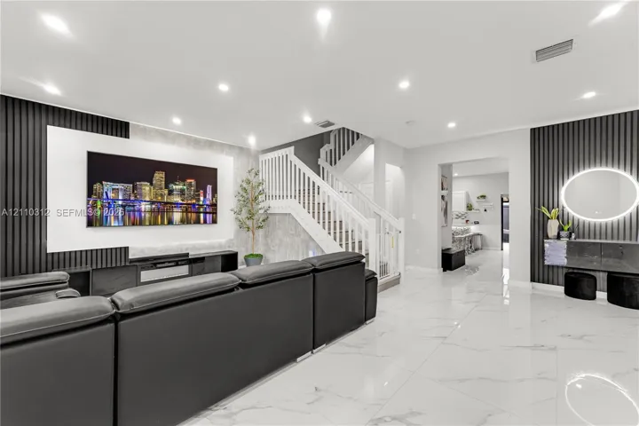 Living area featuring large-format tile flooring, recessed ceiling lighting, vertical slat wall paneling, and a staircase with white wood railings