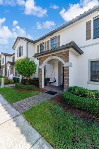 Stucco exterior with stone veneer accents, arched covered entryway, paver walkway, and decorative window shutters