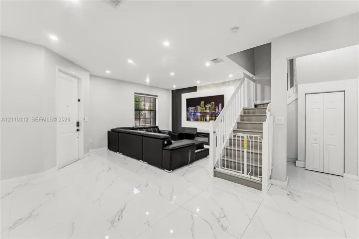 Open floor plan featuring large-format stone-style tile flooring, recessed ceiling lighting, a floor-to-ceiling fireplace surround with stone-finish accent wall, and a staircase with white balusters