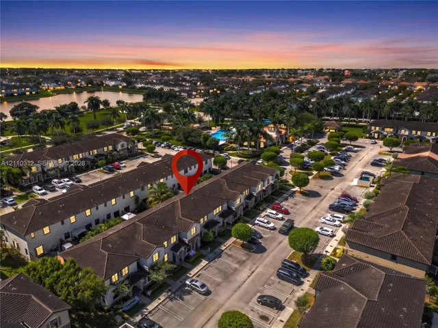 Aerial perspective of multi-story townhome complex featuring a tile roof, dedicated parking spaces, and extensive landscaping