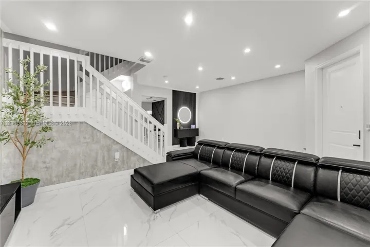Polished tile flooring, recessed lighting, white wood-slat staircase railing, gray stone-finish wall paneling, and a circular LED wall fixture