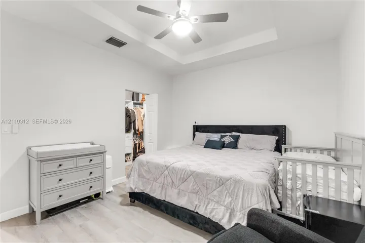 Tray ceiling featuring a central light-integrated ceiling fan, neutral wall finishes, wood-finish flooring, and a walk-in closet with built-in shelving