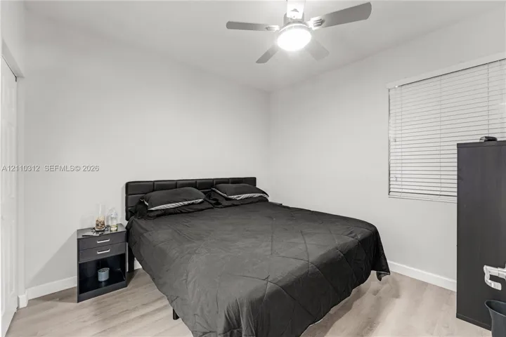 Interior room featuring wood-finish flooring, white walls, horizontal window blinds, and a ceiling fan with integrated light fixture