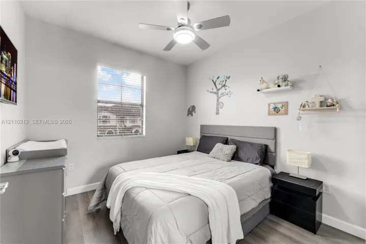 Bedroom featuring wood-finish flooring, a neutral color palette, a single-pane window with horizontal blinds, and a ceiling-mounted light fixture with an integrated fan