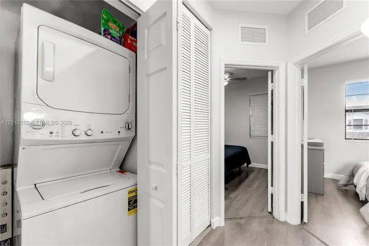 Laundry area featuring a stackable white washer and dryer unit concealed by louvered bi-fold doors