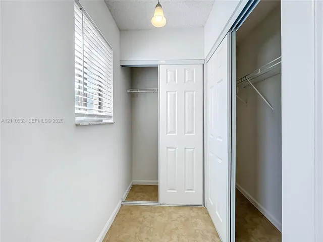 Closet featuring dual sliding panel doors, interior wire shelving, window with blinds, and pendant lighting