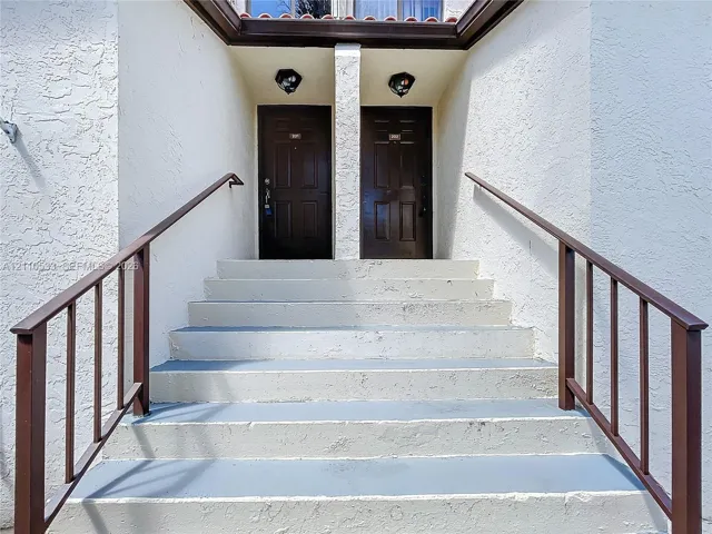 Exterior entrance featuring concrete steps, dual solid wood-finish entry doors, metal handrails, and surface-mounted light fixtures