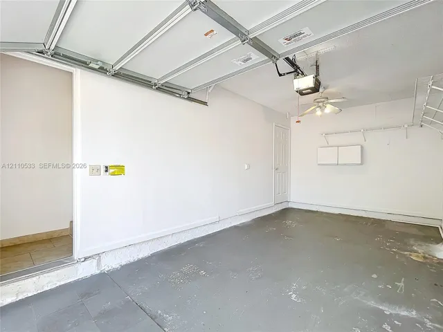 Garage interior featuring an automated overhead door system, ceiling-mounted lighting with an integrated fan, built-in wall shelving, and a painted concrete floor