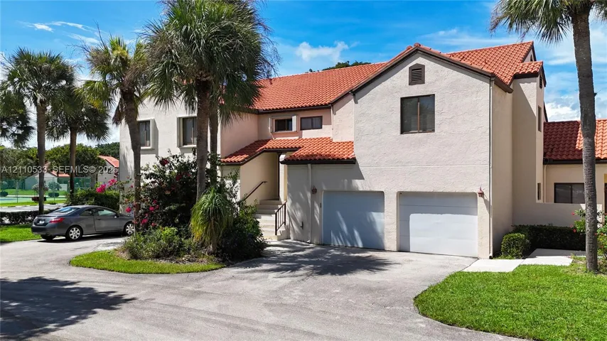 Stucco exterior featuring a dual-car garage and a multi-pitched clay tile roof