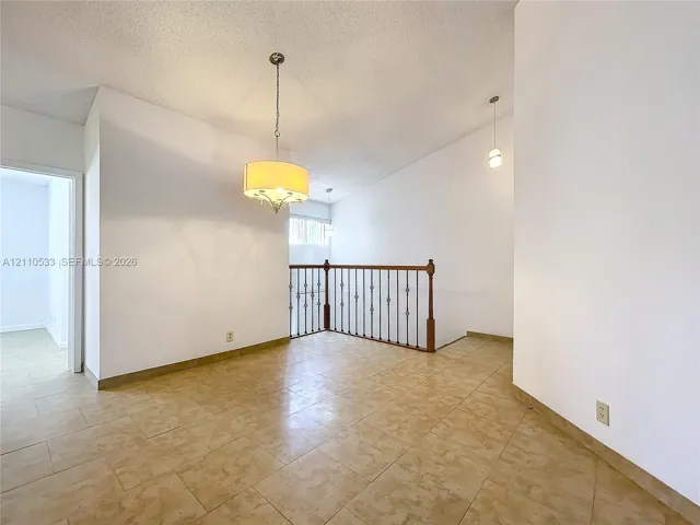 Vaulted ceilings, neutral tile flooring, iron baluster staircase railing, and drum-style chandelier lighting