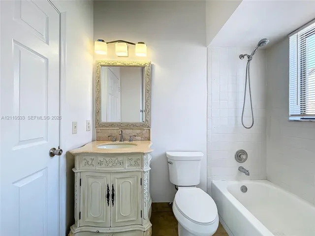 Bathroom featuring an ornate vanity with a stone countertop, an integrated sink, a framed wall mirror, three-light fixture, and a tiled bathtub surround with a handheld shower head