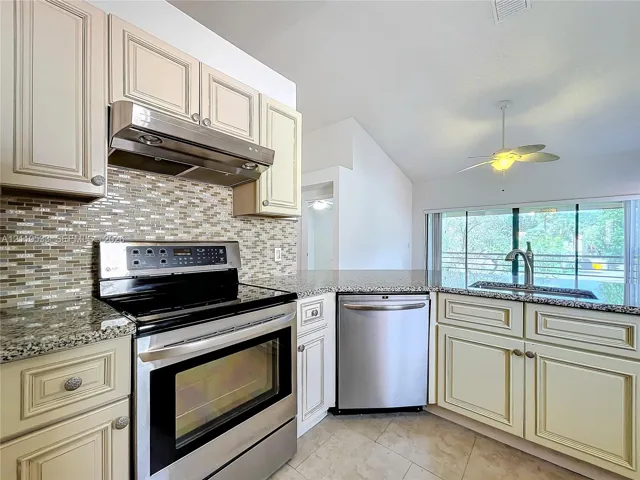 Kitchen featuring shaker-style cabinetry, mosaic tile backsplash, stone-finish countertops, stainless steel appliances, and a vaulted ceiling