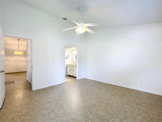 Vaulted ceilings, neutral tile flooring, and a white ceiling fan with integrated lighting